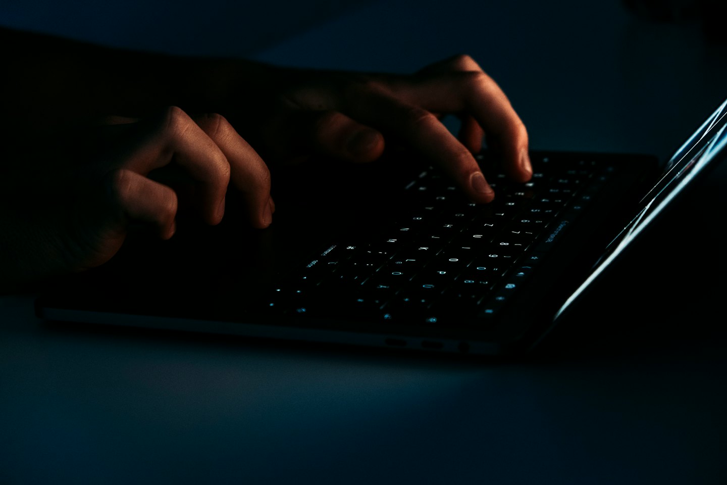 Hands typing on a glowing laptop keyboard in the dark.